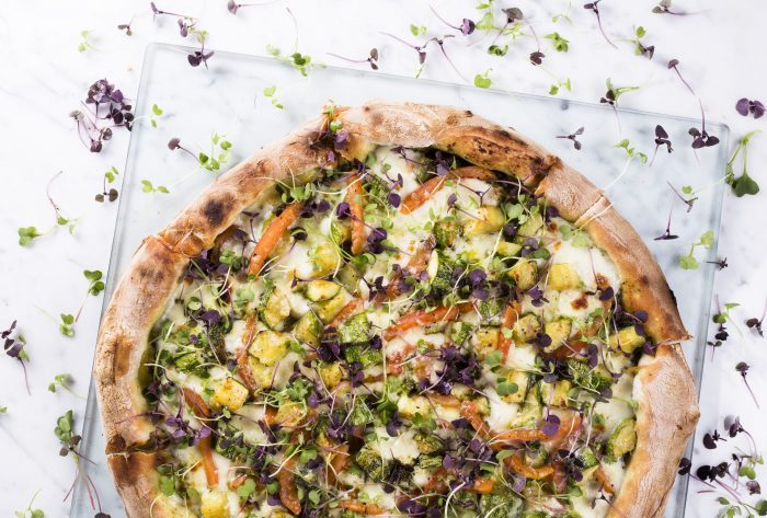 Pizza Zucchine sobre apoio de vidro e mesa branca com flores pelos olhos da fotógrafa Viviane Zatarelli.