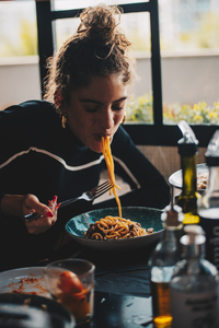 Foto de uma mulher jovem comendo um dos tipos de macarrão italiano.
